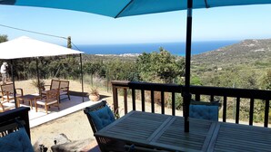 A terrace with a table and chairs, a potted plant, and a view of the sea and hills.