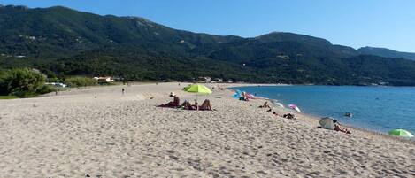 A beach with a clear view of the sea and mountains in the background.