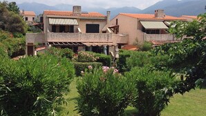 Un edificio in stile mediterraneo, con tetti in terracotta, un cortile ricco di vegetazione e montagne sullo sfondo.