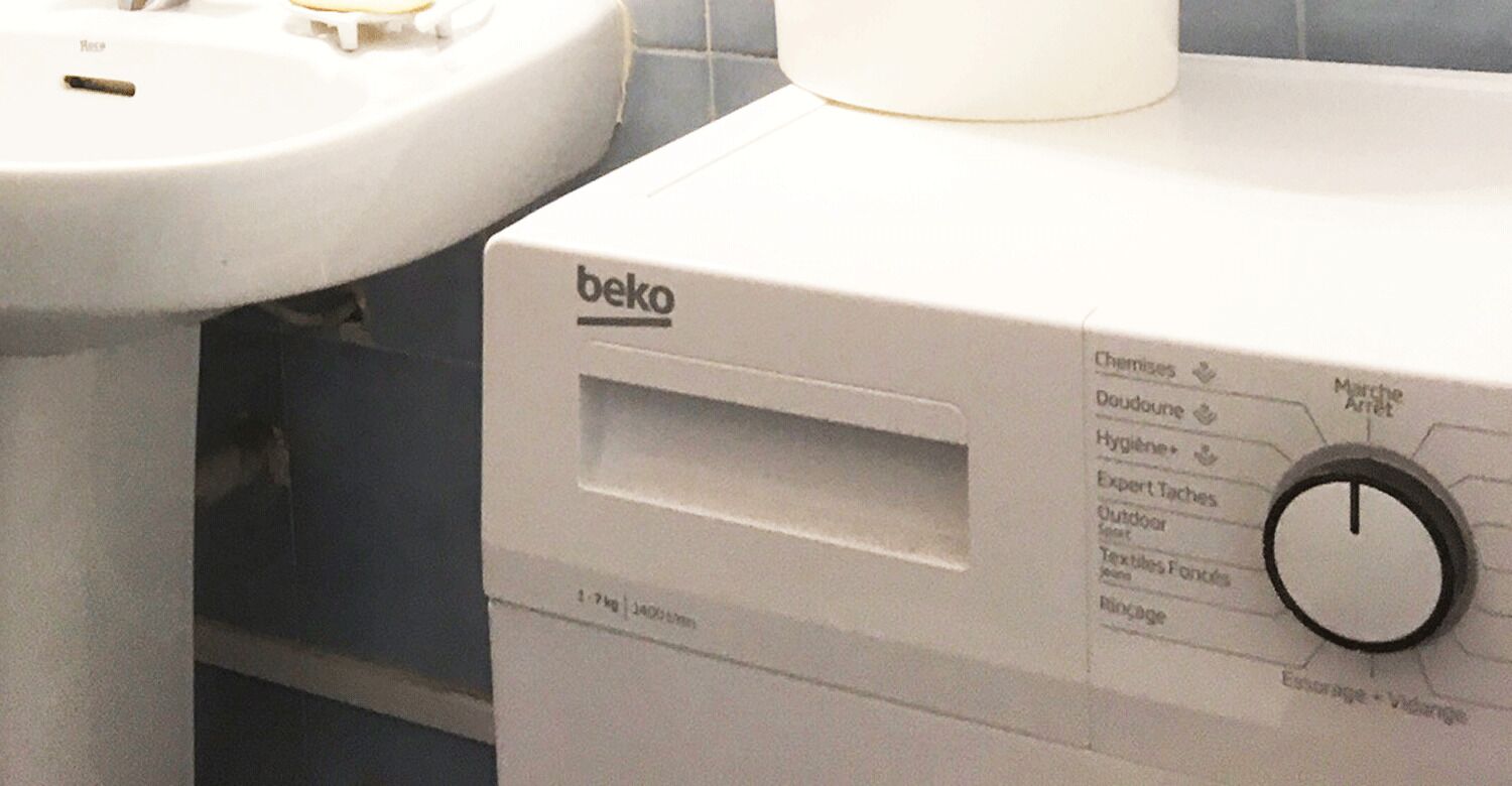 A washing machine with a control panel, a white sink, and a tiled wall.