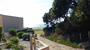 Un giardino con un sentiero che conduce a una spiaggia, un edificio e una recinzione.