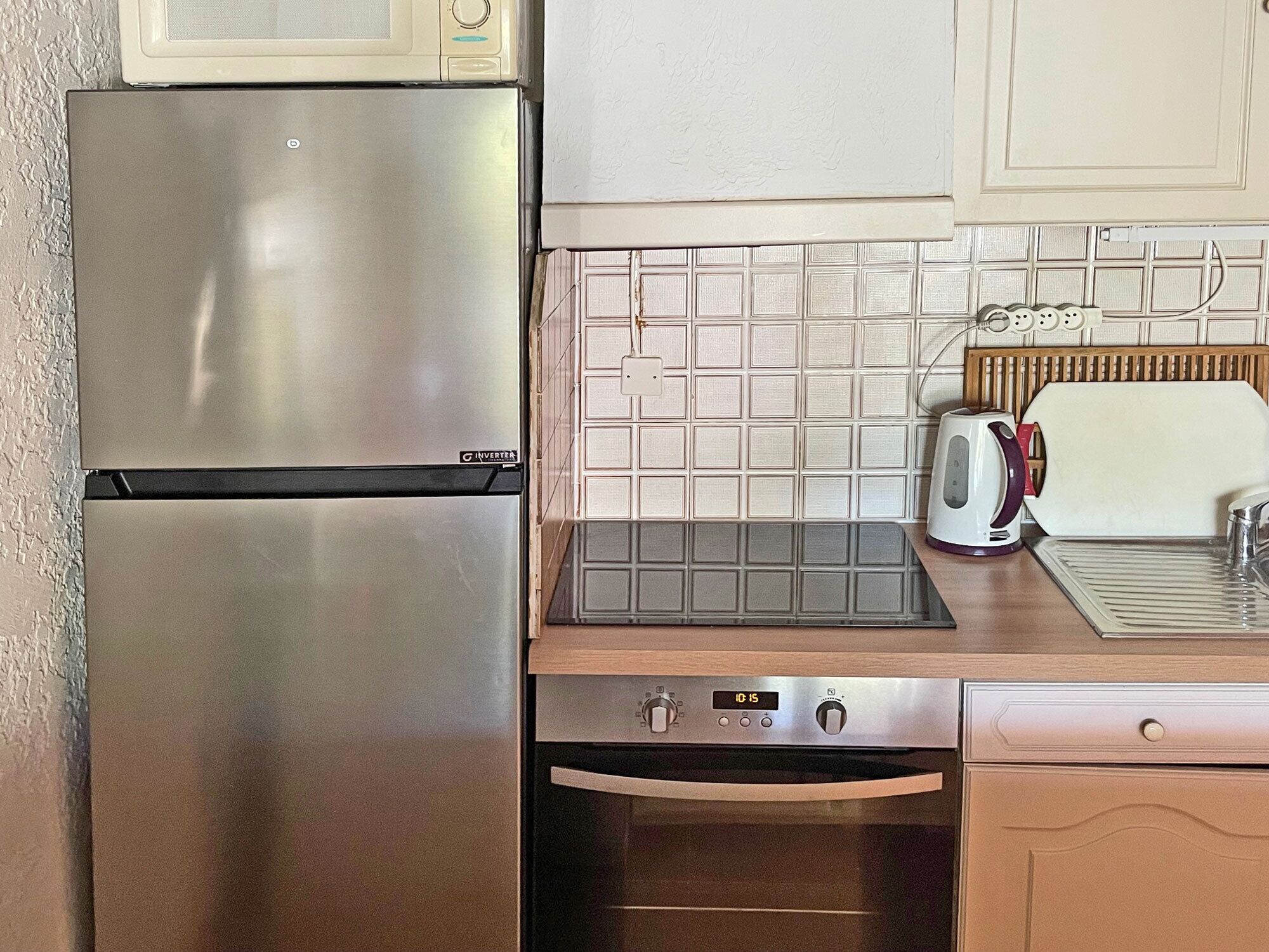Una cocina compacta con refrigerador de acero inoxidable, microondas, tostadora y pileta.