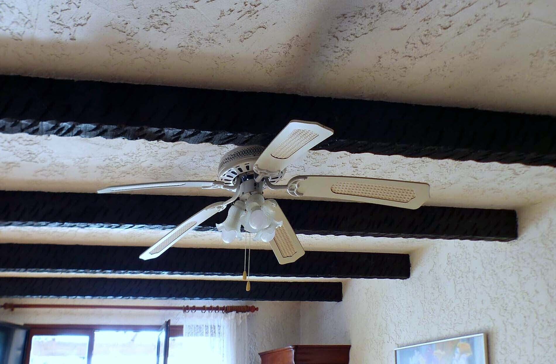 A ceiling fan with a central light fixture in a room with a textured ceiling and dark beams.
