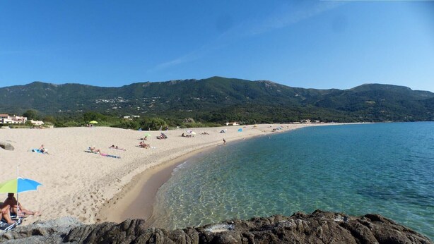 Una spiaggia con acque cristalline, una riva sabbiosa e montagne sullo sfondo.