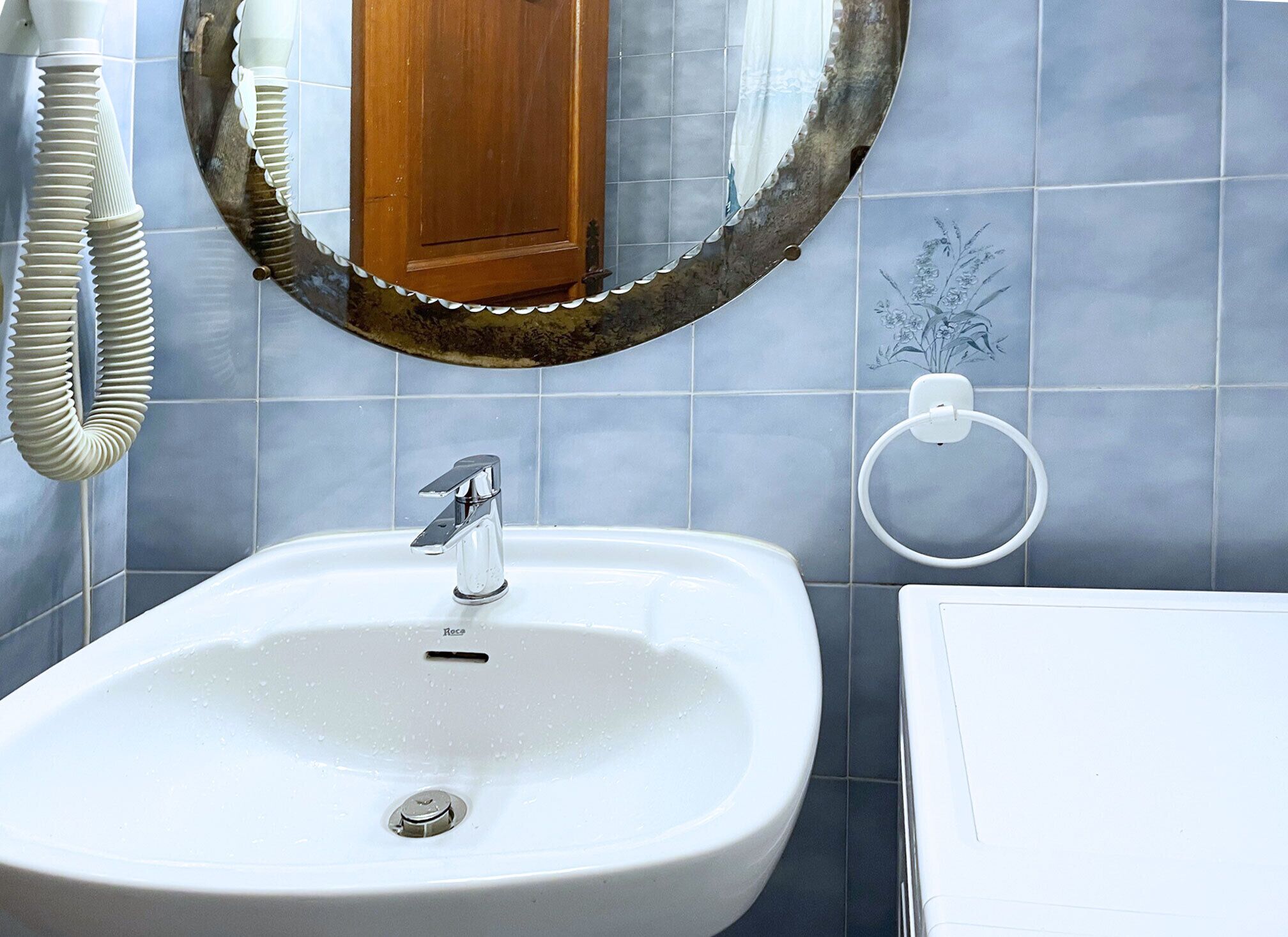 Ein Badezimmer mit einem weißen Waschbecken, einem Spiegel und einem Handtuchhalter an der Wand.