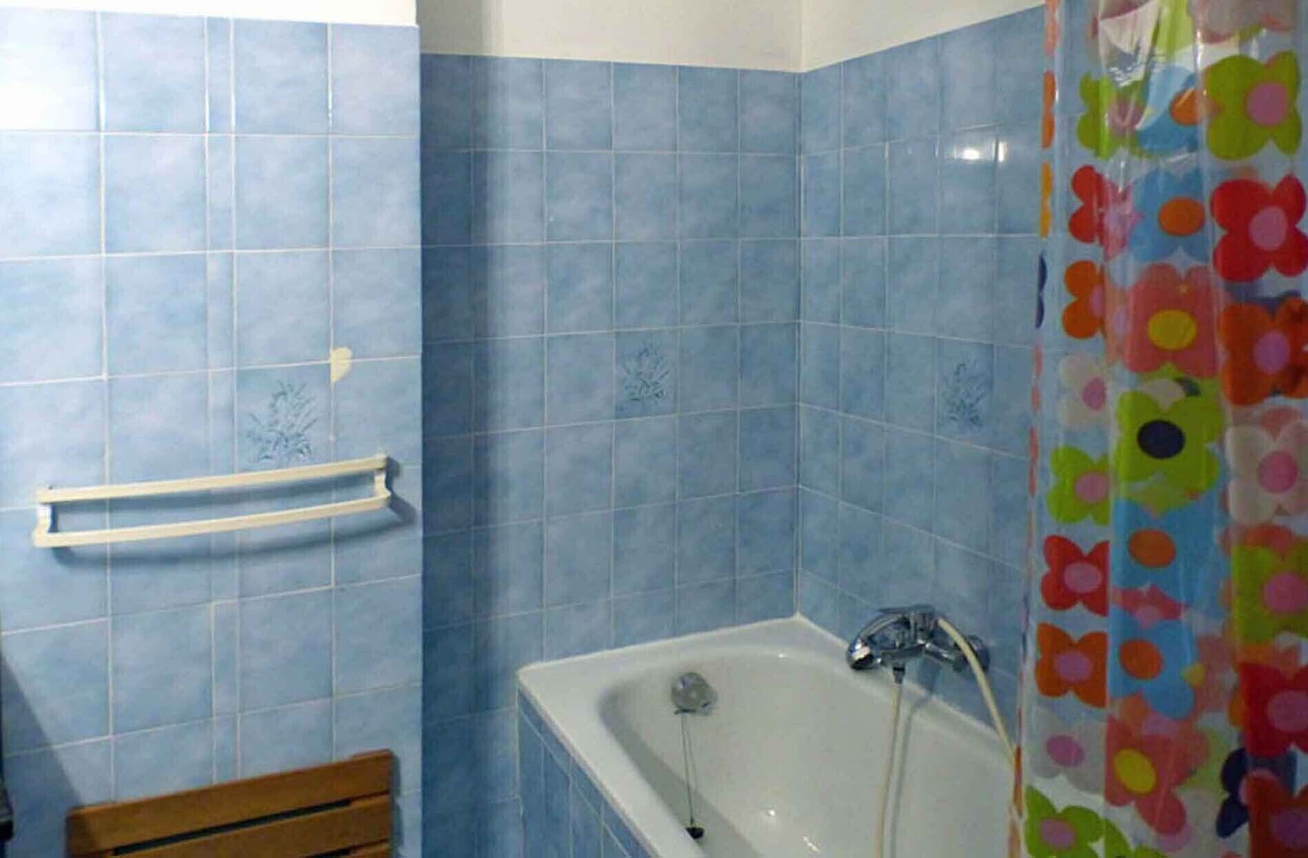 Un bagno con piastrelle blu, una vasca da bagno bianca e una panca in legno.