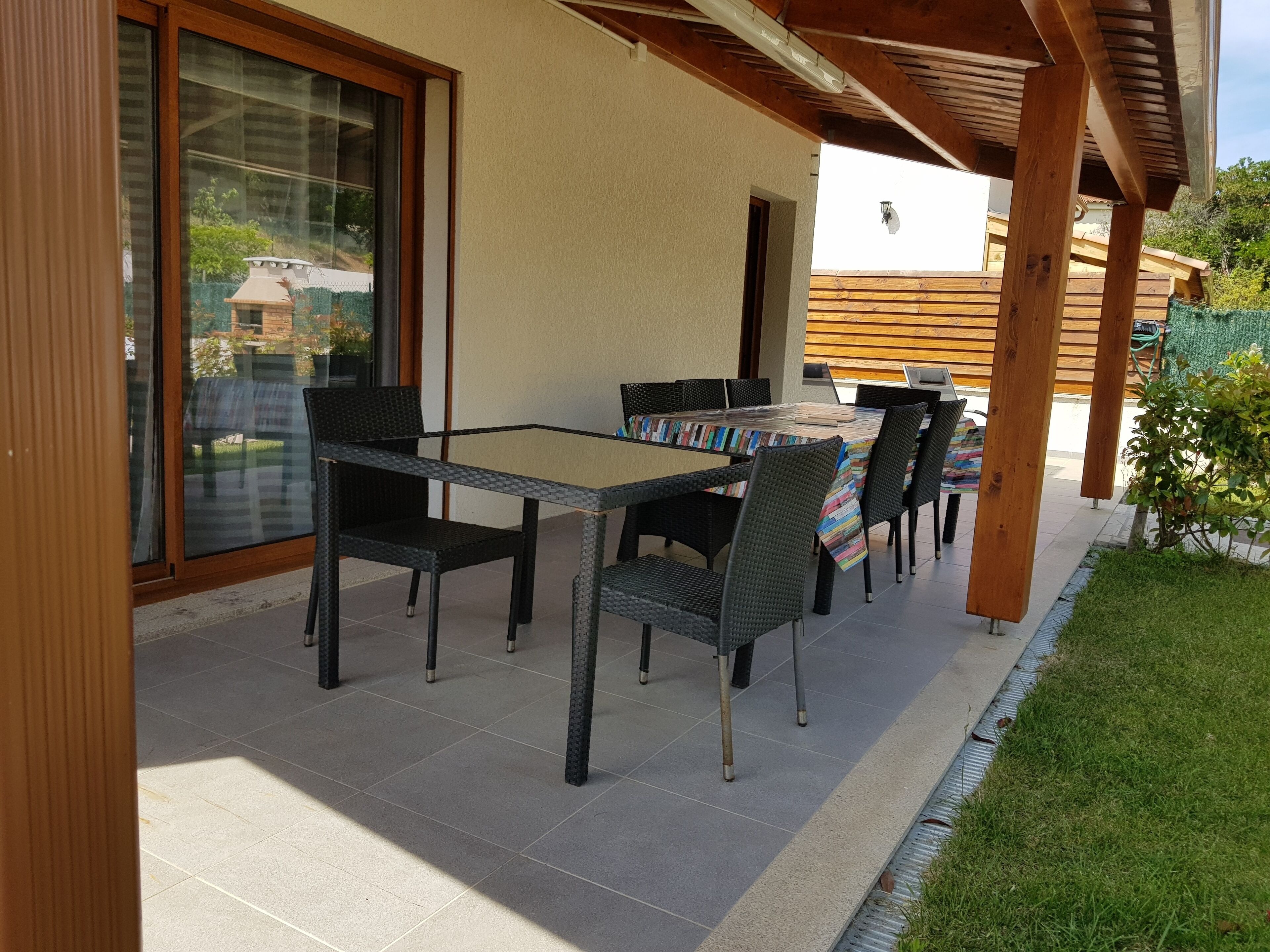Een terras buiten met een tafel, stoelen, een pergola en uitzicht op de omgeving.