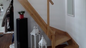 Una scala di legno con una parete bianca e uno specchio. Si vedono lanterne bianche e una pentola rossa su un supporto nero.