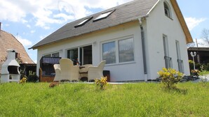 Una casa a due piani con tetto spiovente, ampie finestre e un patio con mobili da esterno.
