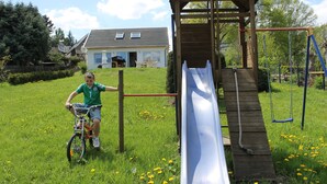 Un bambino in bicicletta nei pressi di un'area giochi con scivolo e altalena.