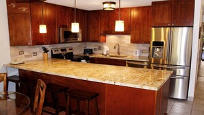 Una cucina moderna con mobili in legno, elettrodomestici in acciaio inossidabile, un piano di lavoro in granito e luci a sospensione.