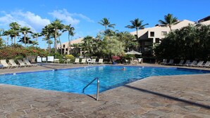 Una piscina con lettini e palme, circondata da edifici.