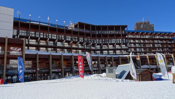 A multi-story building with balconies, a ski shop, and flags.
