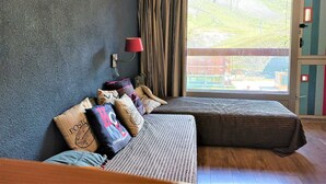 A room with a bed, a nightstand, a lamp, and a view of a building through a window.