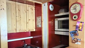 A compact kitchen with wooden cabinets, a sink, a microwave, and a clock.