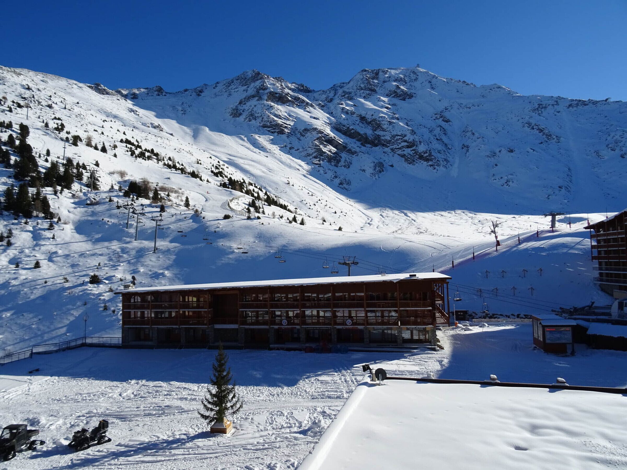 Ein mit Schnee bedeckter Berg mit einer Seilbahn und einer mehrstöckigen Lodge mit großen Fenstern.
