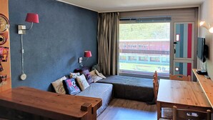 A cozy room with a blue wall, a wooden bench, a sofa with cushions, a table, and a TV on the wall.