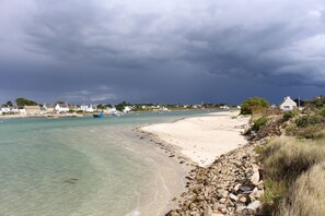 A coastal landscape with a clear beach, rocky shoreline, and calm sea.