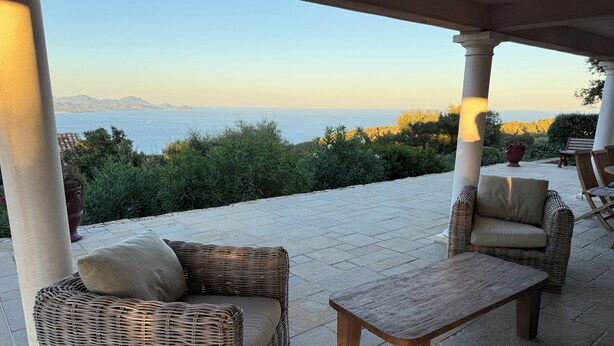 An outdoor patio with wicker furniture, a stone table, and a view of the sea.