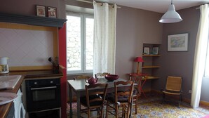 Une cuisine avec une table à manger, des chaises et une lampe rouge. On y trouve une fenêtre avec des rideaux, un lave-linge et une cuisinière.