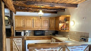 A rustic kitchen with wooden cabinets, a brick-patterned counter, and a hanging light fixture. - Cottage rental between Cahors and St Cirq Lapopie (Arcambal)