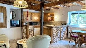 A rustic kitchen with wooden cabinets, a brick wall, and a dining area with a table and chairs. - Cottage rental between Cahors and St Cirq Lapopie (Arcambal)