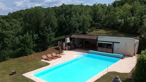 A swimming pool with lounge chairs, a covered patio, and a statue in a landscaped backyard. - Cottage rental between Cahors and St Cirq Lapopie (Arcambal)