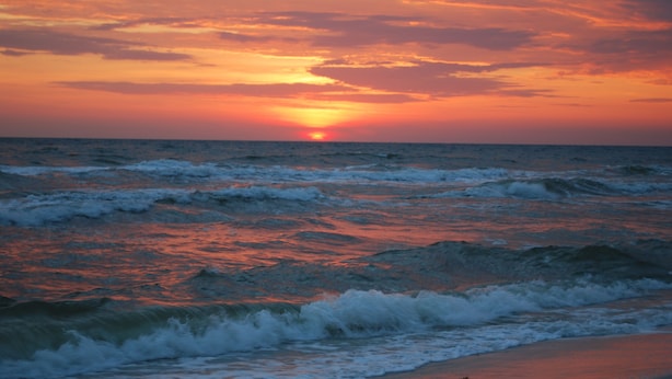 Un atardecer sobre el océano con olas rompiendo en la orilla.