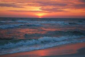 Een zonsondergang boven de oceaan met golven die op het strand breken.