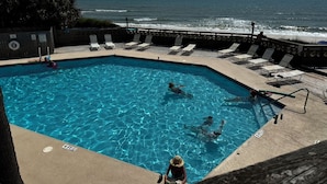 Una piscina con agua cristalina azul, rodeada de sillas de descanso y una terraza de madera.
