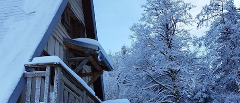 A wooden cabin with a snow-covered roof and a wooden staircase leading to a balcony.