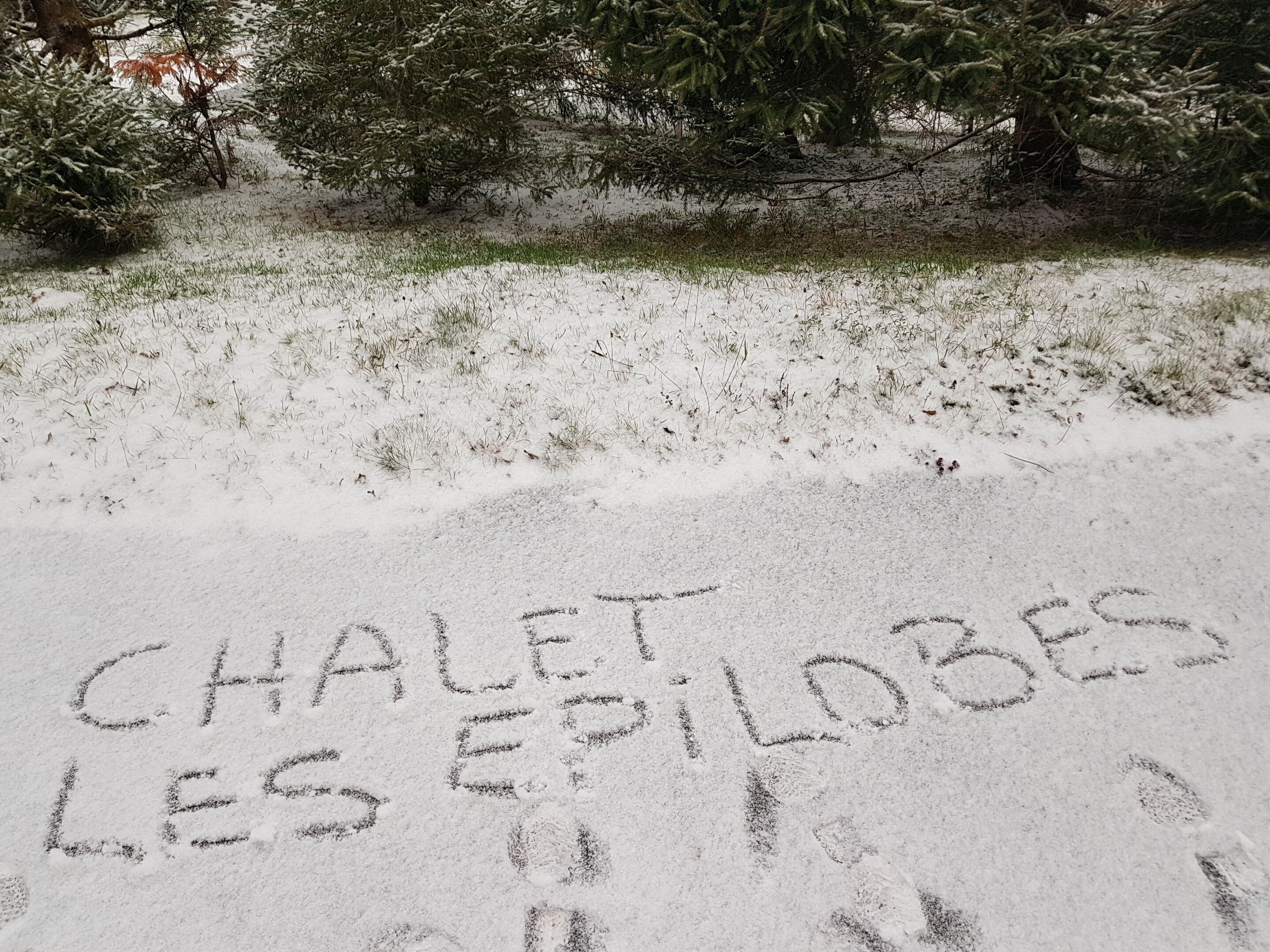 A snow-covered ground with the words "CHALET LES EPILOBES" written in the snow.