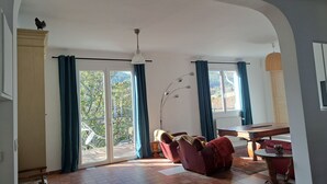 Een ruime woonkamer met een schuifdeur naar een balkon, een rode bank, een houten tafel en een plafondventilator.