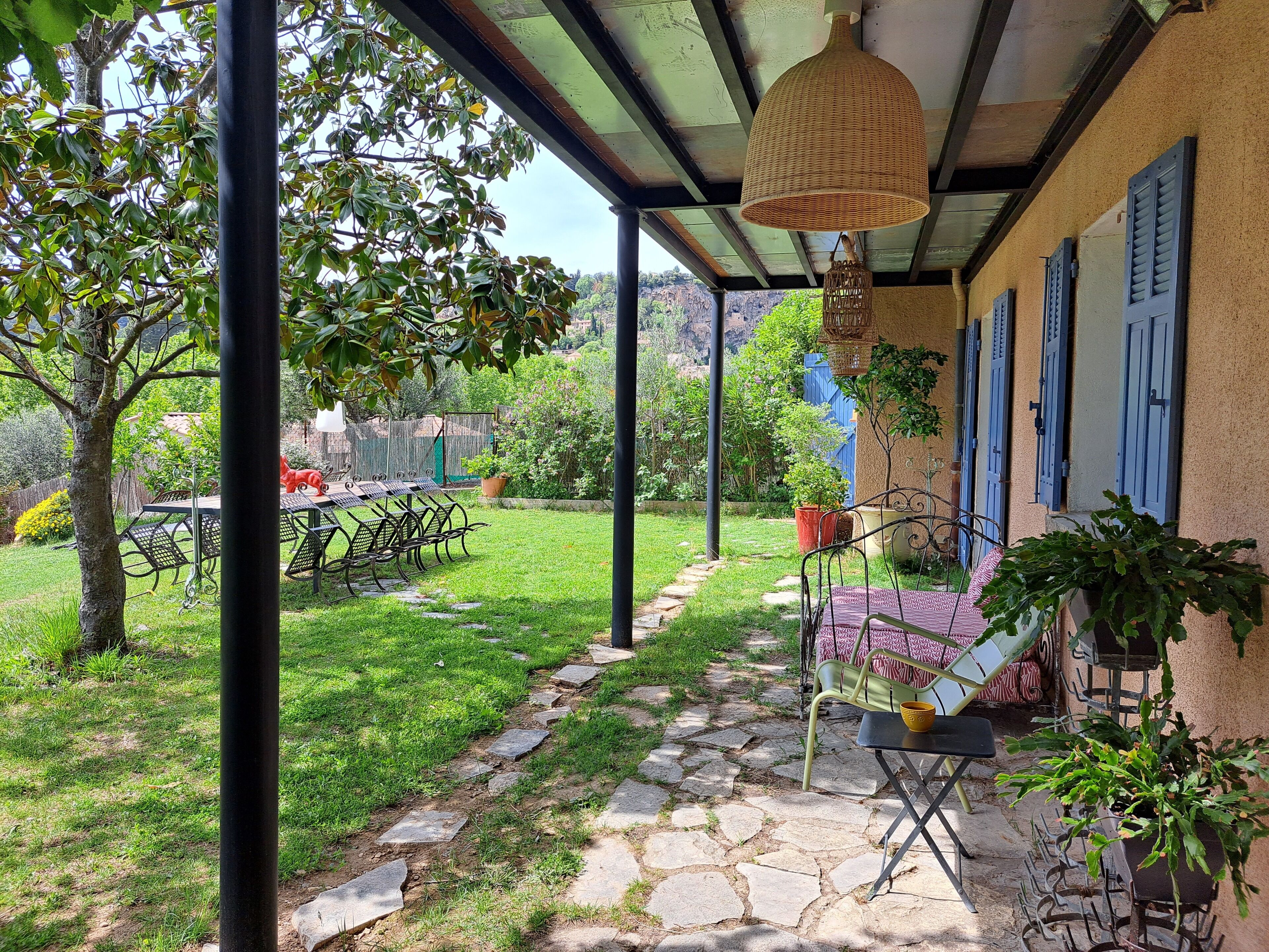 A covered patio with a stone pathway, outdoor furniture, and potted plants.