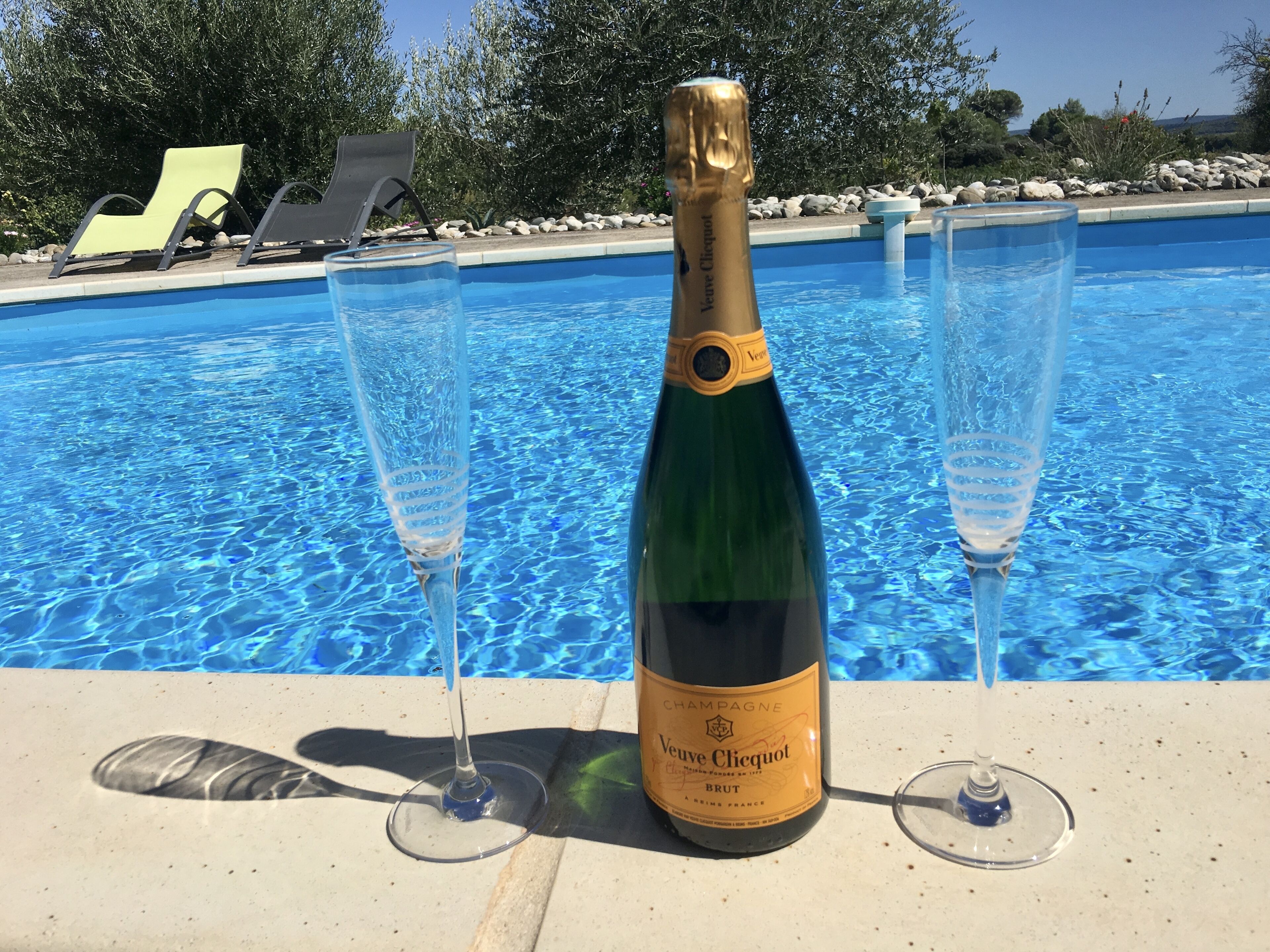 Una botella de champán Veuve Clicquot y dos copas junto a una piscina.