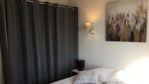 A bedroom with a large bed, a dark curtain, a wall-mounted lamp, and a painting. - Quiet cottage + pool, for 3 pers. (Lézignan-Corbières)