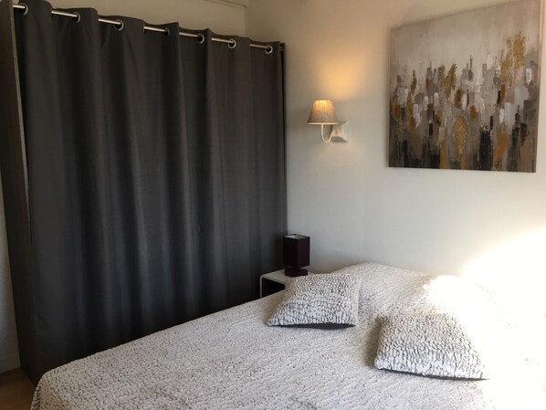 A bedroom with a large bed, a dark curtain, a wall-mounted lamp, and a painting. - Quiet cottage + pool, for 3 pers. (Lézignan-Corbières)