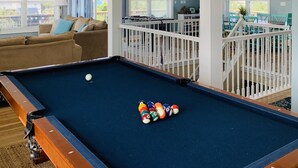 Une table de billard avec des billes, un canapé et une vue sur un balcon avec des sièges d’extérieur.