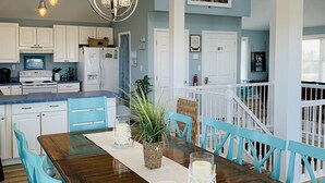 Une cuisine spacieuse avec des meubles blancs, une table à manger en bois et des chaises de couleur turquoise.