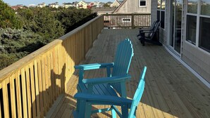 Une terrasse en bois avec deux chaises Adirondack bleues, une clôture en bois et une vue sur des maisons au loin.