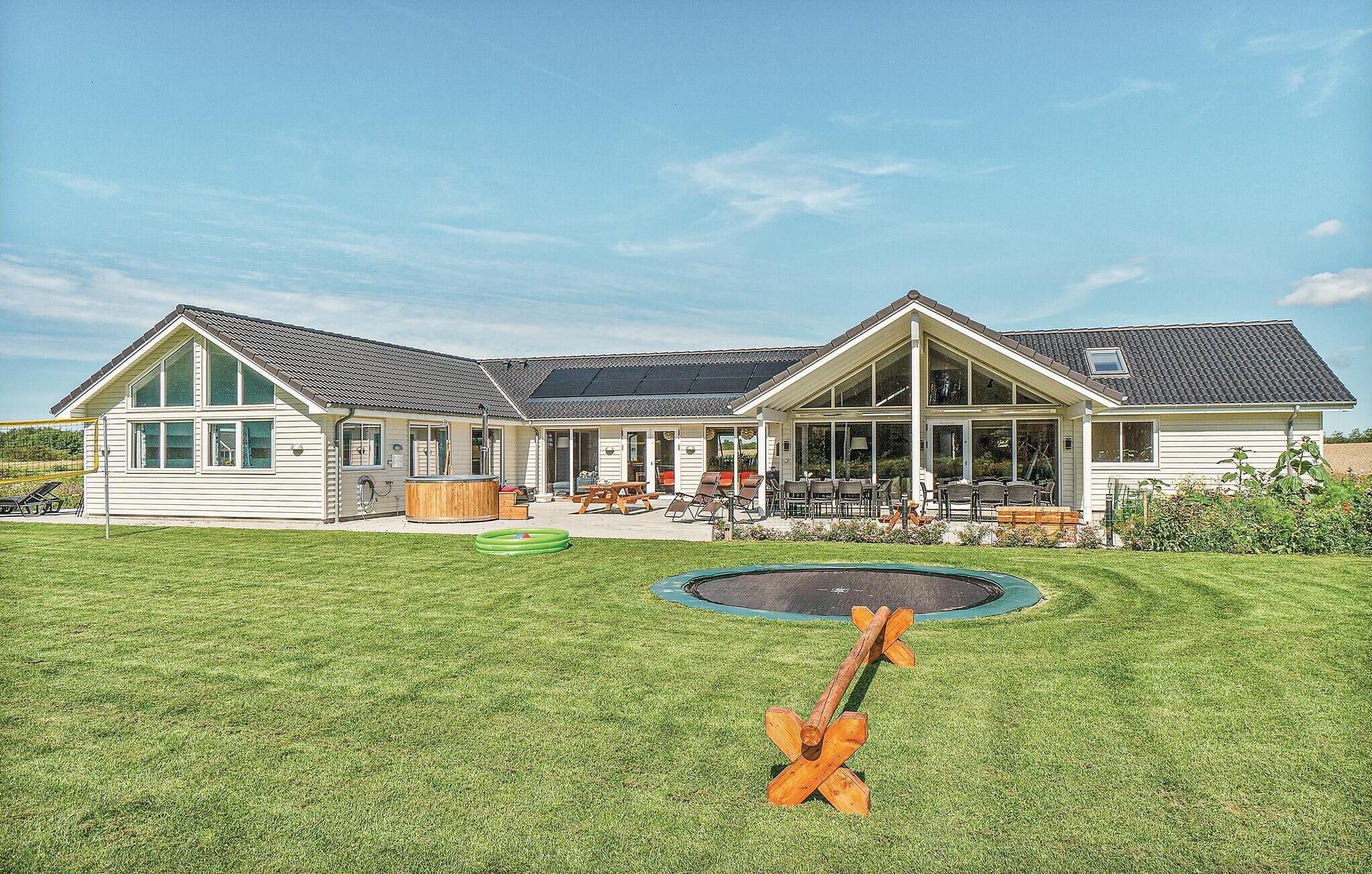 Une maison à deux étages avec un patio couvert et un trampoline dans le jardin.
