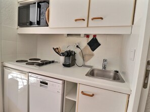 A compact kitchen with a dishwasher, stove, and a microwave above the counter. - Studio 4 pers, west balcony, Méribel (Méribel)