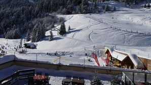 A snow-covered ski resort with a chairlift, ski slopes, and a wooden building with a sign.