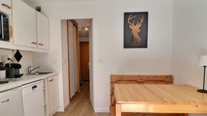 A kitchen with white cabinets, a dishwasher, and a dining area with a wooden table and bench.
