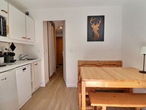 A kitchen with white cabinets, a dishwasher, and a dining area with a wooden table and bench.