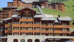 A multi-story wooden lodge with balconies, a stone facade, and a ski lift in the background.