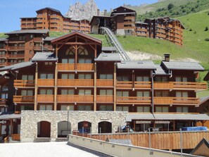 A multi-story wooden lodge with balconies, a stone facade, and a ski lift in the background.