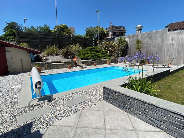 A swimming pool with a stone border, surrounded by a garden with various plants and a stone wall.