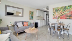 A modern living room with a grey sofa, a round wooden coffee table, and a dining area with metal chairs and a wooden table.