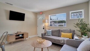 A modern living room with a flat-screen TV, a sofa, a coffee table, and a side table with a lamp.